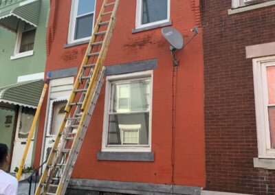 Before photo of a Philadelphia, PA brick rowhome with faded peeling red painted brick facade and extension ladders set for exterior repainting by UMAR Painting Co.
