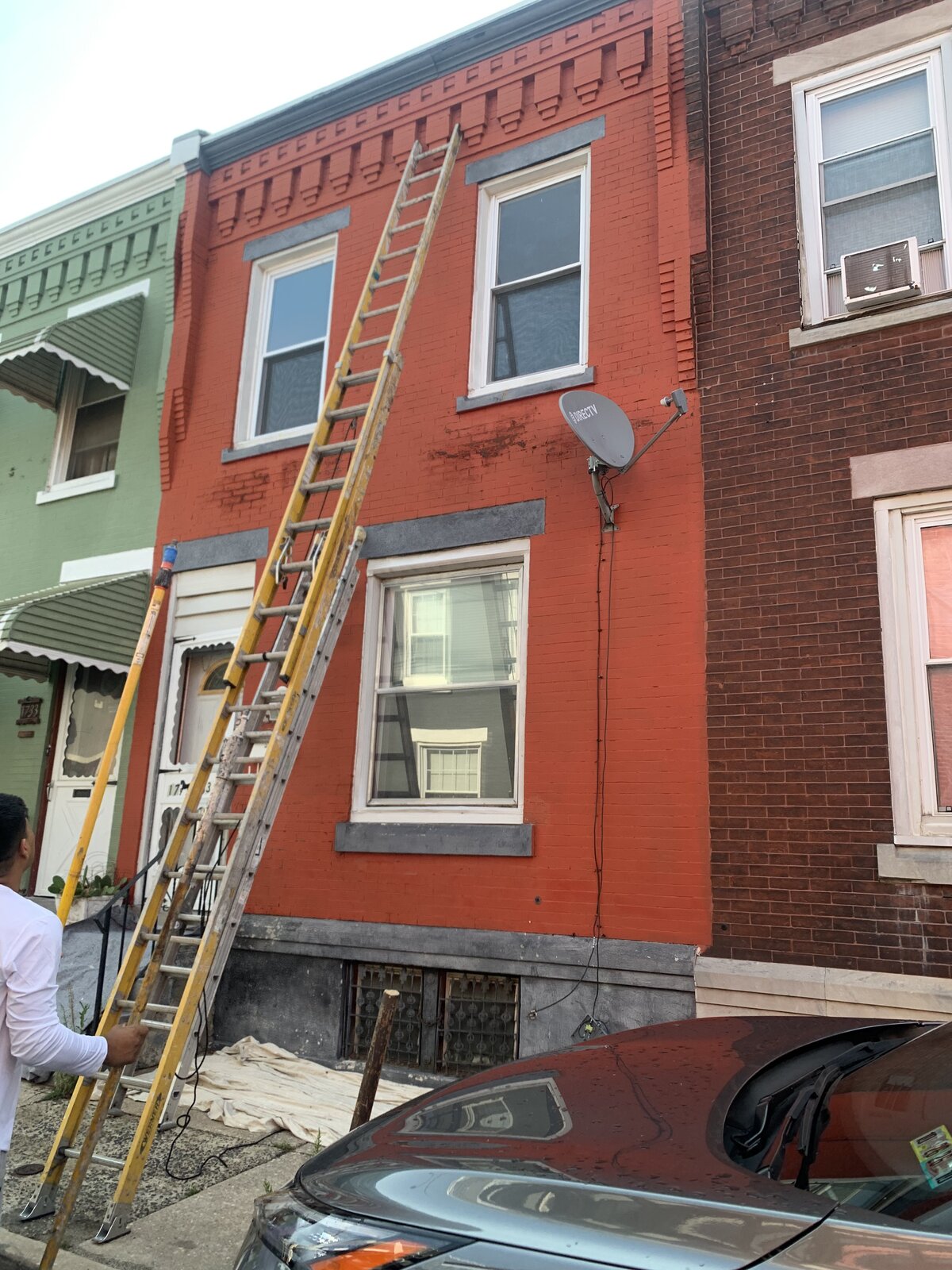 BEFORE — Faded Red Brick Rowhome Facade, Philadelphia, PA | Affordable Philly Painters Before photo of a Philadelphia, PA brick rowhome with faded peeling red painted brick facade and extension ladders set for exterior repainting by UMAR Painting Co.