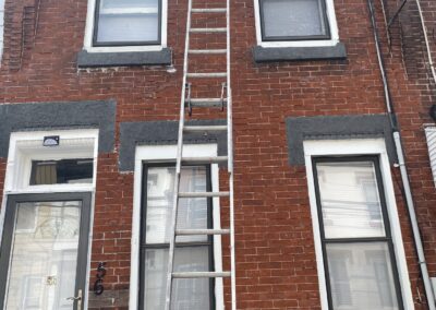 Exterior brick rowhouse painting Philadelphia with ladder positioned for trim work