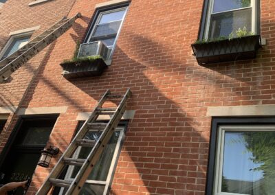 Ladders positioned for exterior window trim painting on a Philadelphia brick rowhouse