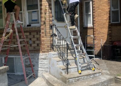 Painters preparing and coating white porch trim on a Philadelphia brick home