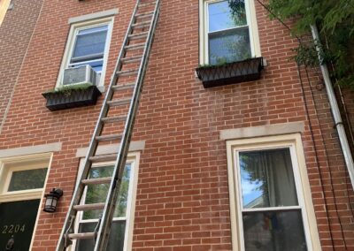 Extension ladder and painter at a Philadelphia brick rowhouse exterior trim project