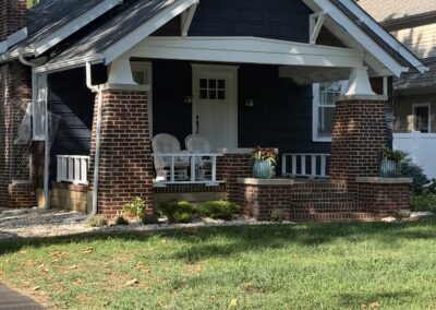 After exterior repaint: craftsman bungalow front elevation painted deep navy blue with white trim and gable brackets over red brick porch columns in Philadelphia, PA, by UMAR Painting Co.
