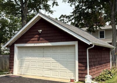 Before exterior painting: faded maroon cedar shake detached two-car garage with a white overhead door in Philadelphia, PA, prior to work by UMAR Painting Co.