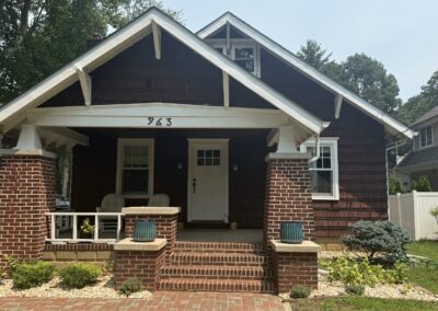 Before exterior repaint: dark maroon cedar shake craftsman bungalow front elevation with red brick porch columns in Philadelphia, PA, prepared by UMAR Painting Co.