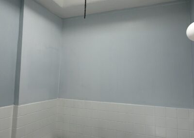 After photo of a repaired and repainted bathroom with smooth light blue walls and ceiling above white tile wainscot in a Philadelphia, PA rowhome, finished by UMAR Painting Co.