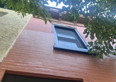 After photo looking up a freshly painted terracotta rowhome facade with black window trim and a new white cornice in Philadelphia, PA, painted by UMAR Painting Co.