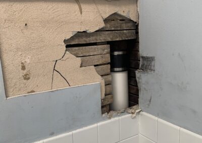 Before photo of a hole cut in a plaster bathroom ceiling above white tile to access a drain pipe in a Philadelphia, PA rowhome, before drywall patching and painting by UMAR Painting Co.