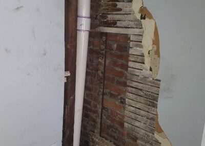 Before photo of failed plaster and wood lath exposing the brick party wall and a new PVC drain line in a Philadelphia, PA rowhome, prior to plaster repair and repainting by UMAR Painting Co.
