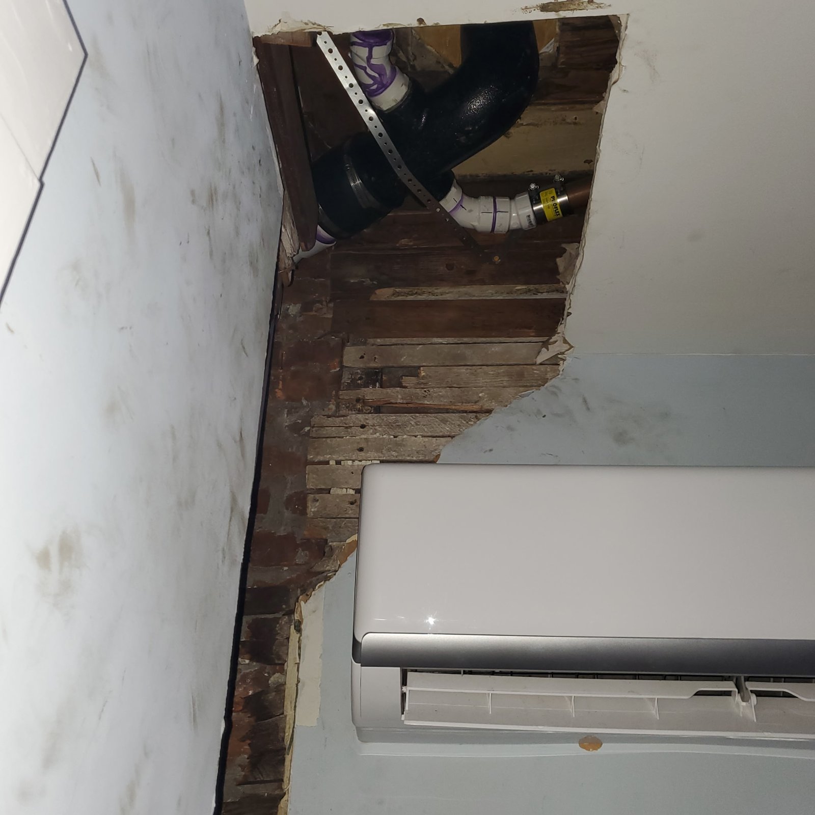 Before Drywall Repair - Exposed Lath and Brick Around Mini-Split Line Set, Philadelphia, PA | Affordable Philly Painters Before photo of damaged plaster with exposed wood lath, brick and cast iron pipe above a wall-mounted mini-split unit in a Philadelphia, PA home, before drywall repair and painting by UMAR Painting Co.