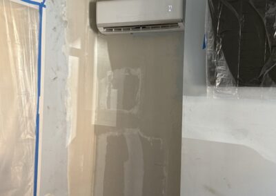 In-progress photo of a skim coated and sanded drywall repair around a wall-mounted mini-split in a Philadelphia, PA home, masked and ready for primer and paint by UMAR Painting Co.