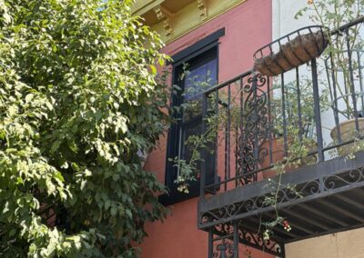 Exterior painting of a Philadelphia, PA rowhome facade in terracotta with black window trim, black wrought iron balcony and gold cornice details by UMAR Painting Co. exterior painters